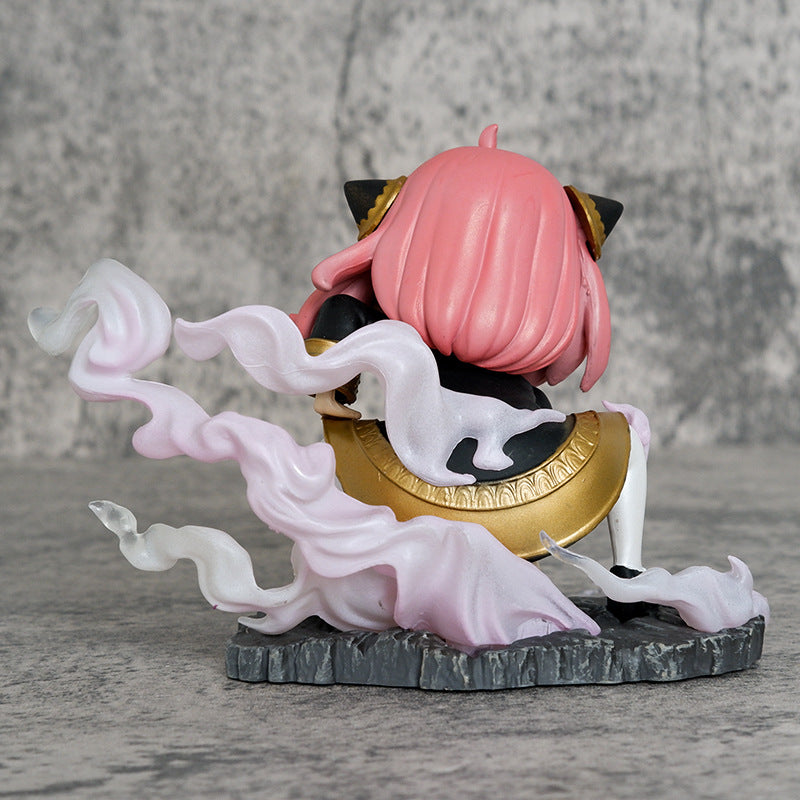 The Spy x Family Anya Forger PVC Figure, featuring pink hair and black cat ears, sports a gold-accented outfit while seated on a rocky base. White trails encircle the figure against a gray backdrop. This 9.5 cm figure offers a double head replacement in Luffy Cosplay by Spy × Family.