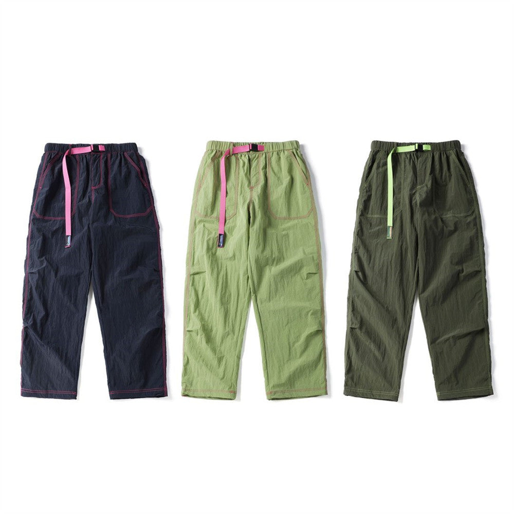 Three pairs of crinkled parachute pants in navy, light green, and olive with contrasting drawcords