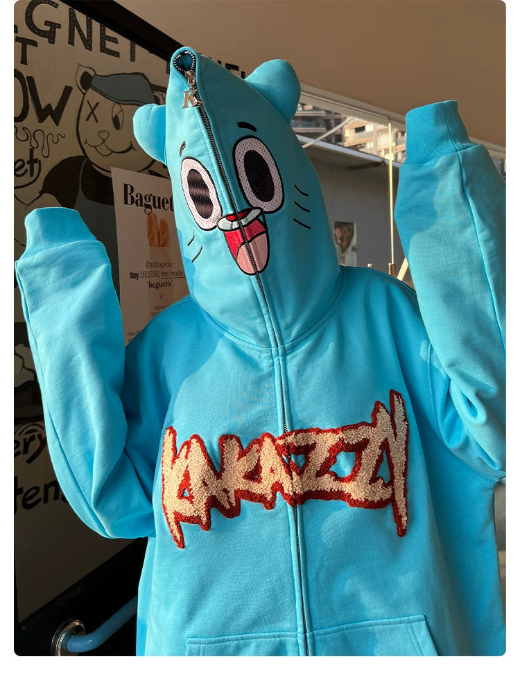 A person wears the Adorable Blue Cartoon Hoodie by Seakoff, a 400GSM cotton hoodie featuring a playful bear face design on the hood. This oversized hoodie is light blue with &quot;KARAZY&quot; in bold letters and fully zips up for an intriguing look.