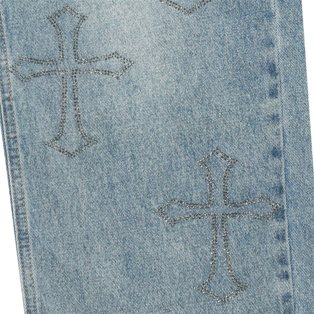 Close-up of light blue jeans leg with rhinestone cross embroidery