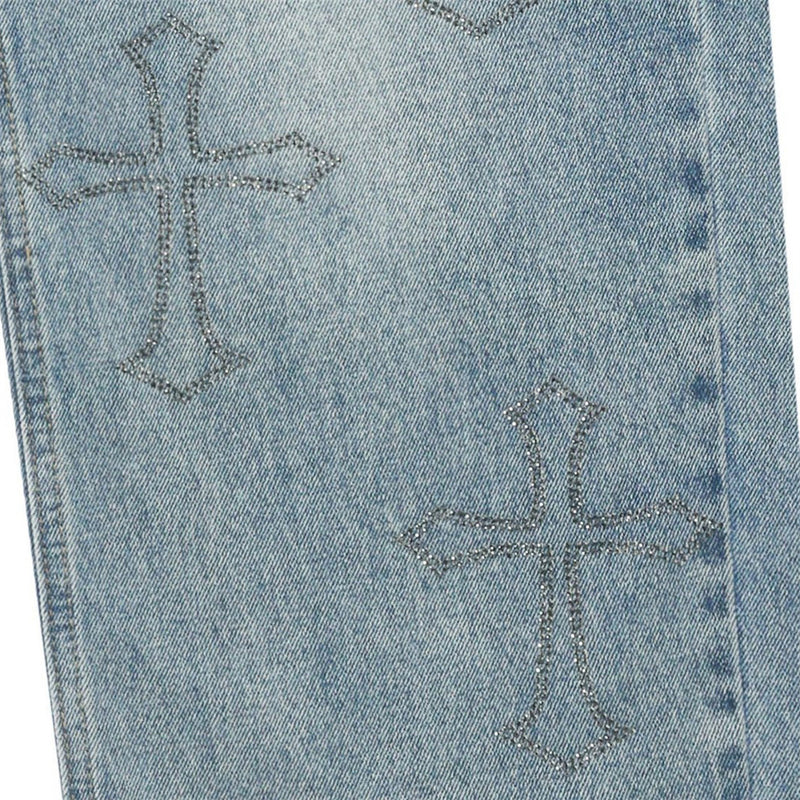 Close-up of light blue jeans leg with rhinestone cross embroidery