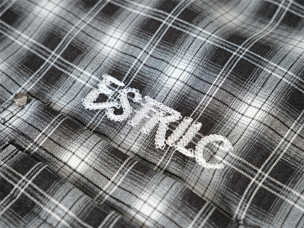 Close-up of white embroidered logo on black plaid shirt fabric