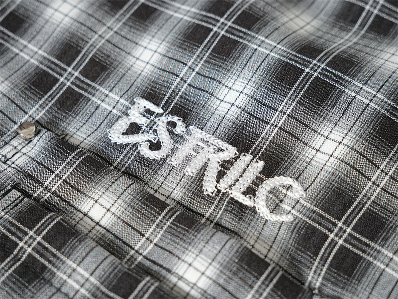 Close-up of white embroidered logo on black plaid shirt fabric