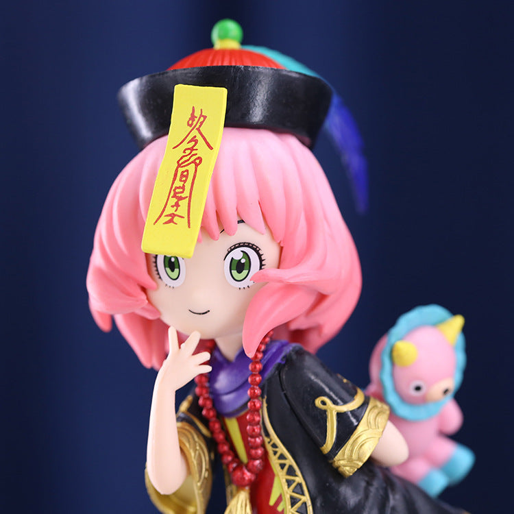 A vibrant Spy × Family PVC figure of Anya Forger in her school uniform features pink hair, green eyes, a playful expression, a black hat with a yellow tag, and gold-accented attire while cradling a small blue unicorn-horned creature on her shoulder.