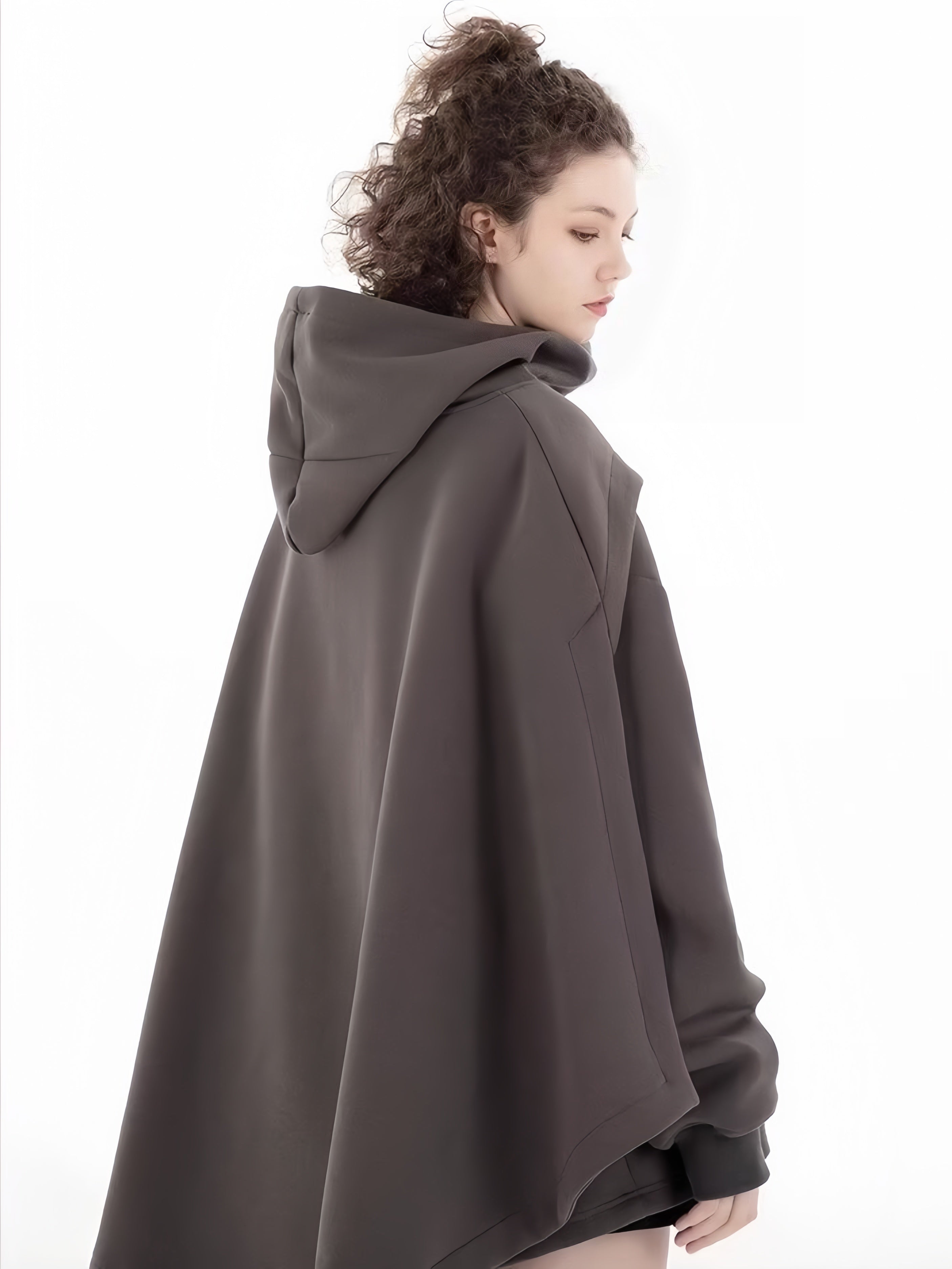 A person with long curly hair wears a Limited Edition Attack on Titan Hooded Cape – Street Style. Against a plain white background, the thick and comfortable cape subtly enhances their attire as they look to the side.