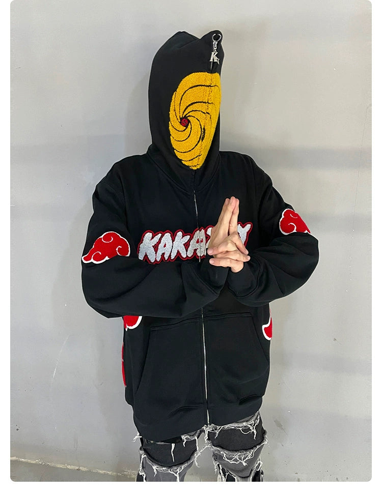 A person wearing a Seakoff Uchiha Obito-Inspired Hoodie, featuring an Akatsuki Cloud Design with a Spiral Mask, stands cross-armed against a plain wall. Paired with ripped jeans, the look perfectly captures the essence of dedicated Naruto fans.