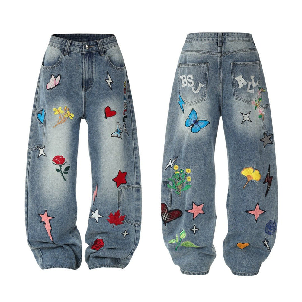 Wide-leg washed blue denim jeans with colorful embroidered patches including roses, butterflies, stars, and lightning bolts,