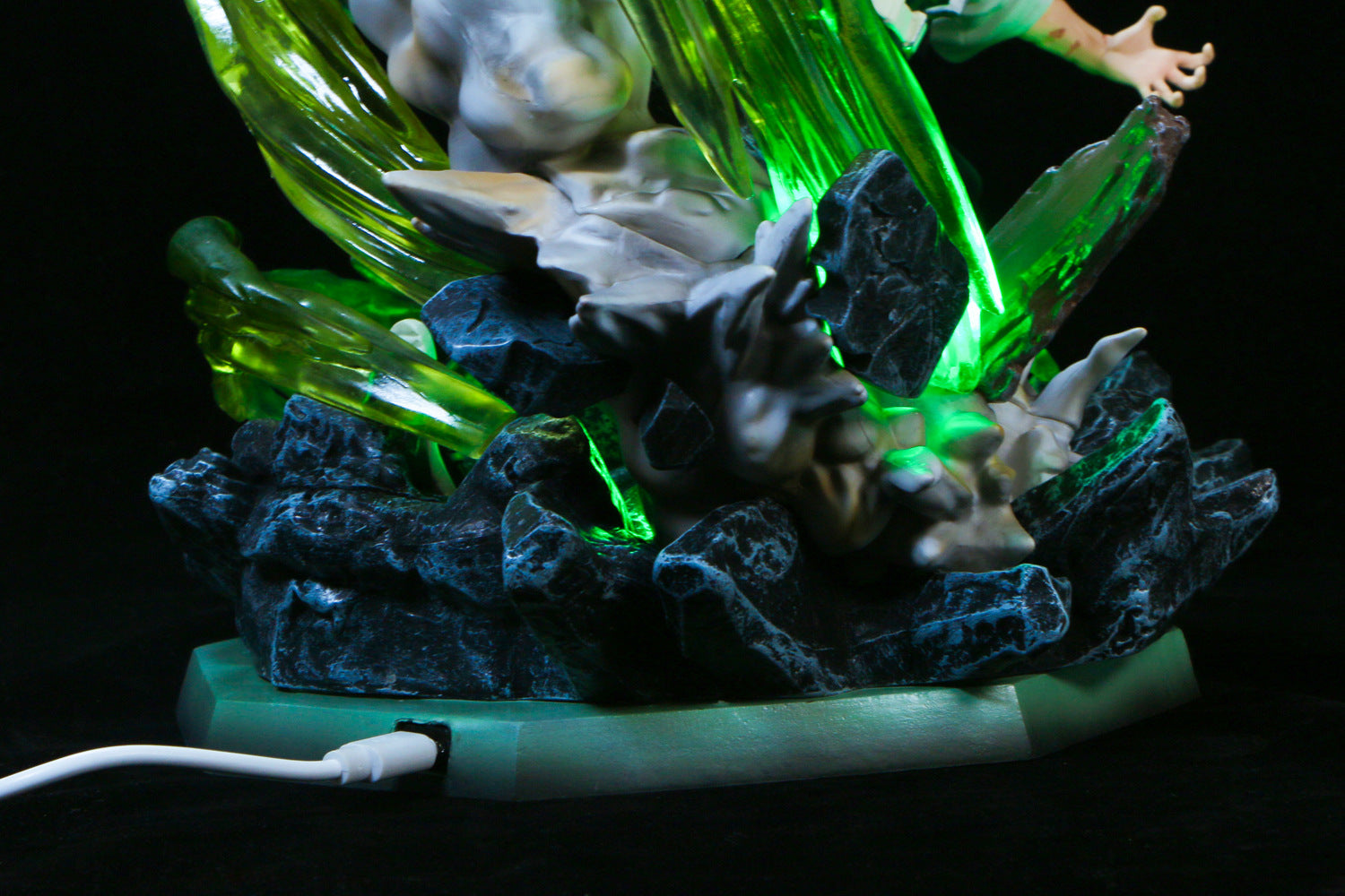 The Premium Demon Slayer Kaze Hashira Sanemi Shinazugawa Figure is a 30cm high-quality GK model featuring jagged dark and green translucent elements illuminated from within. It rests on a green base with a visible USB power cord at the bottom left, partially covered by a human hand on the upper right.