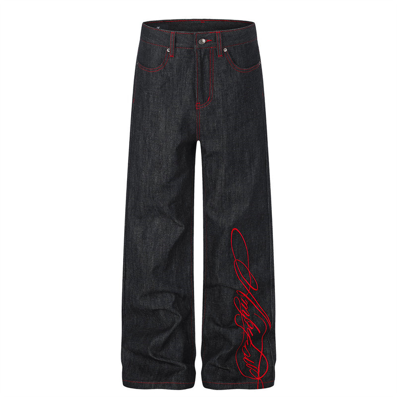 Jean homme noir à jambes larges en denim brut, avec surpiqûres rouges et broderie cursive rouge sur le bas de la jambe, vue de face et de dos