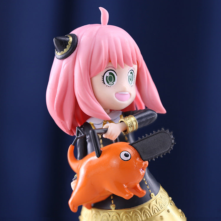 The Anya Forger Chainsaw Cosplay Figure by Spy × Family features pink hair, green eyes, and a black horn. Dressed in a dark outfit with gold trim, she holds an orange cartoon dog and a chainsaw against a dark blue backdrop—ideal for any Spy × Family collector.