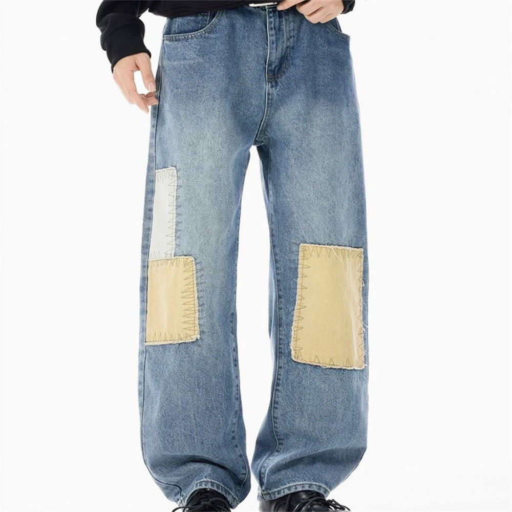 Men's washed blue wide-leg straight fit jeans with contrast off-white and tan patchwork appliqués and zigzag stitching on fro