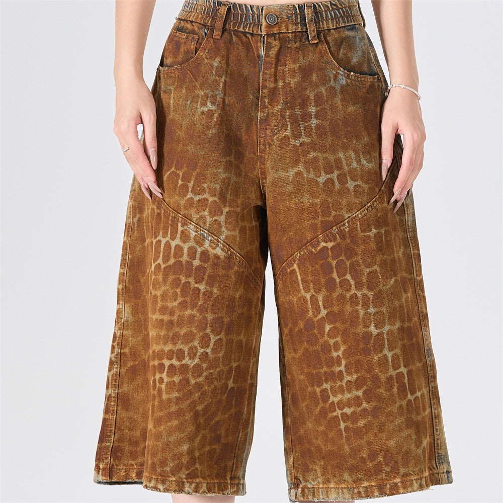Wide-leg denim shorts in distressed rust brown leopard scale spray-dye print with front seam paneling and mid-rise waist