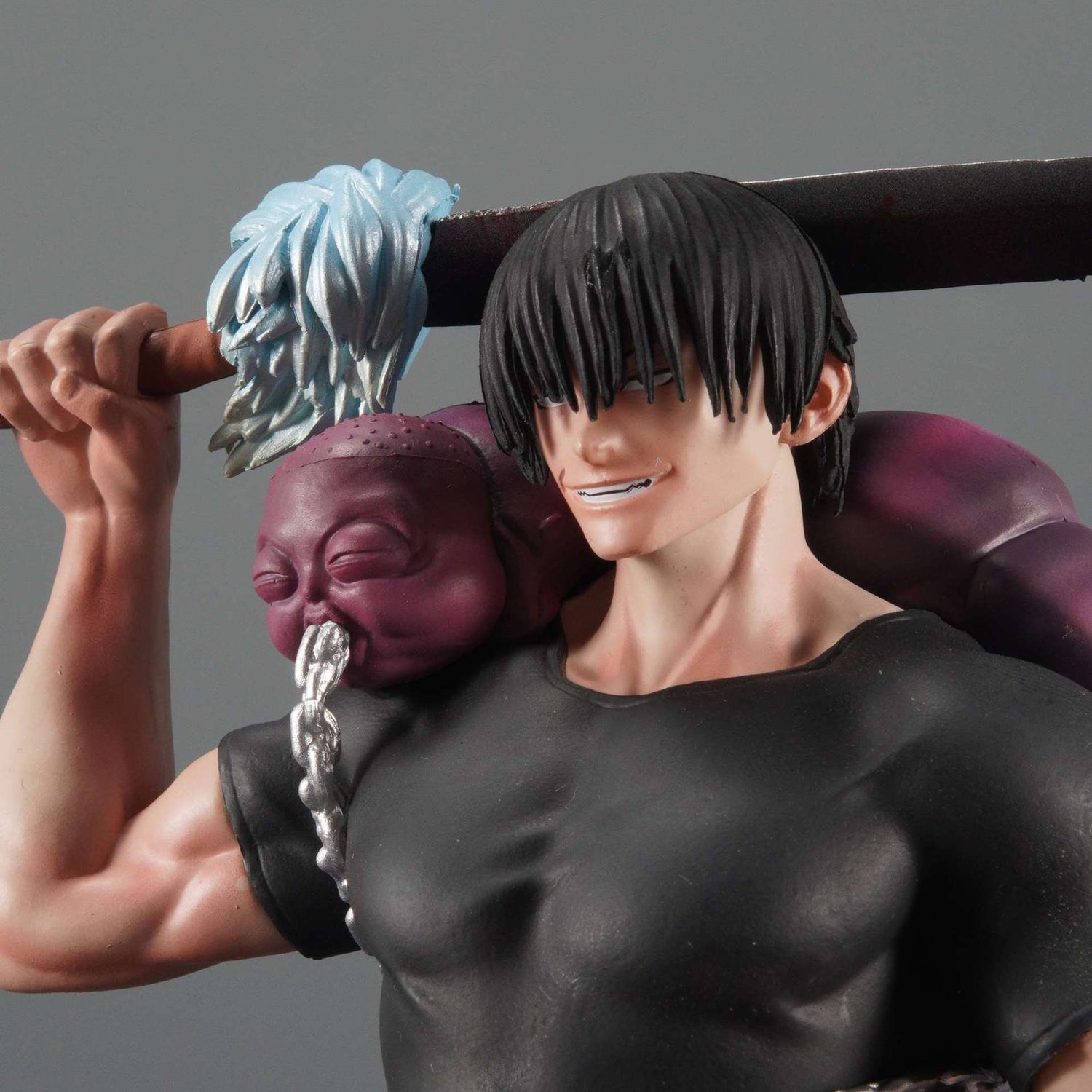 The &quot;Jujutsu Kaisen Fushiguro Toji PVC Figure – 21 cm&quot; features a dynamic action pose with long black hair and a sinister smile, holding a sword over the shoulder. A purple, chained head with light blue hair enhances this collectible statue, wearing a black shirt against a plain gray background.