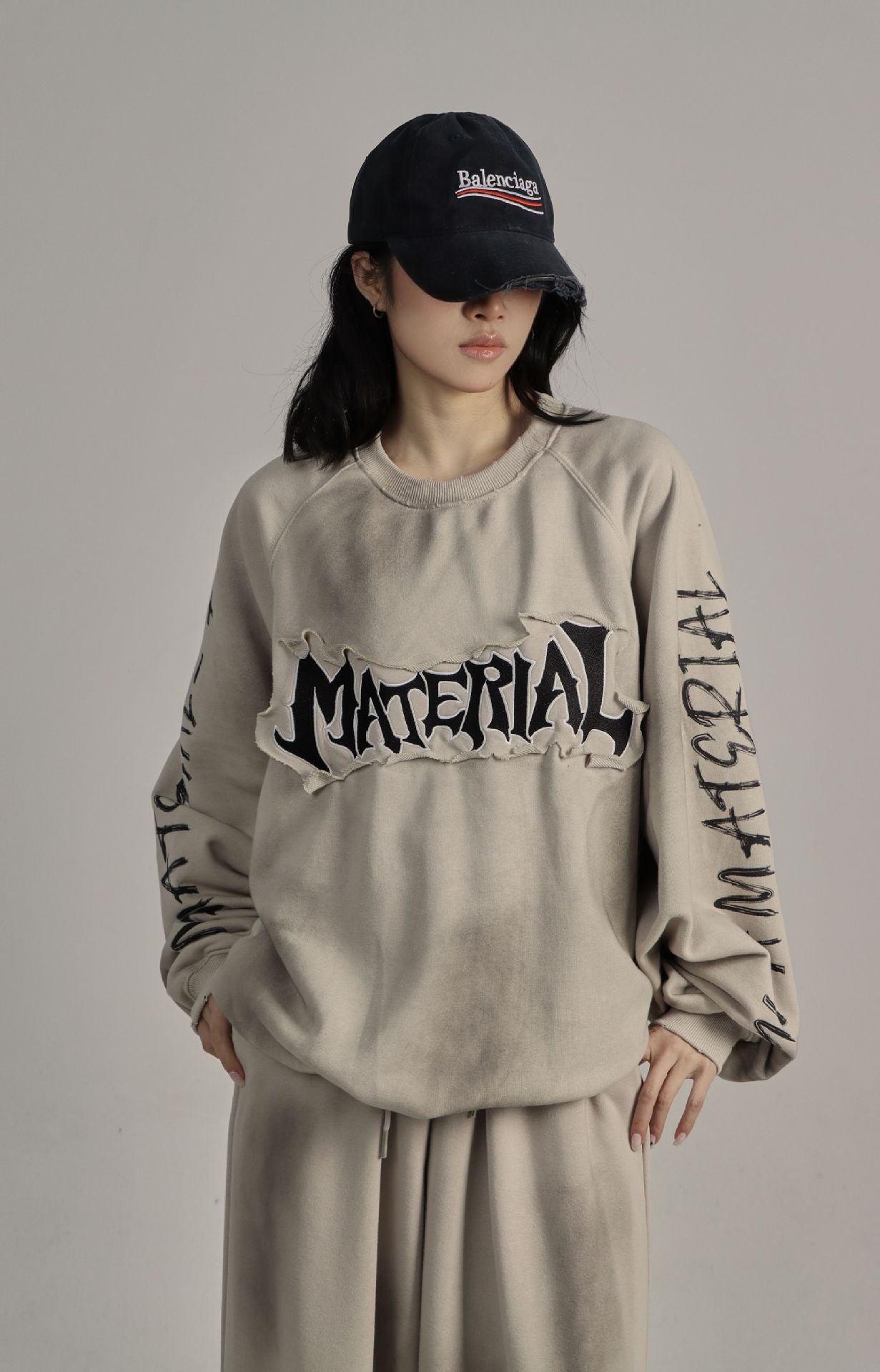 Oversized men's crew neck sweatshirt with distressed 'Material' gothic patch appliqué and washed sand beige finish, styled wi