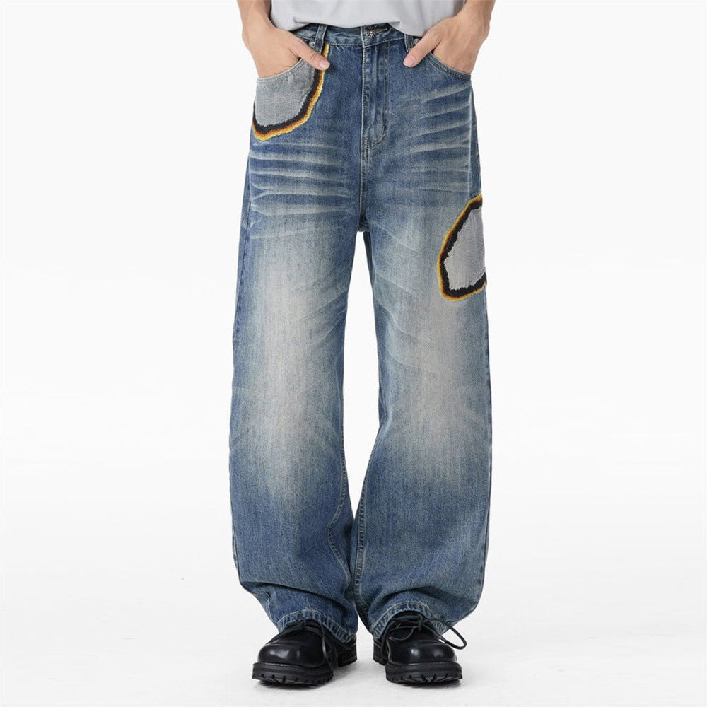 Men's baggy straight-leg distressed blue jeans with black and yellow embroidered patch appliqués on front thigh and pocket