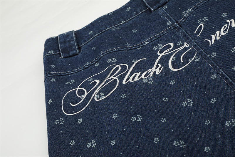Close-up of script embroidery on the back of dark blue floral print jeans