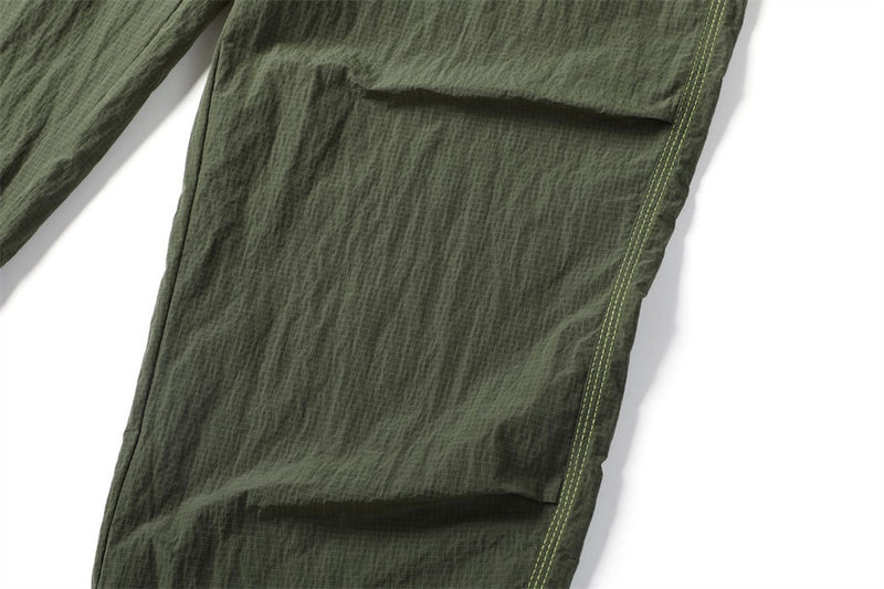 Close-up of an olive parachute pants cargo pocket flap and double green stitching