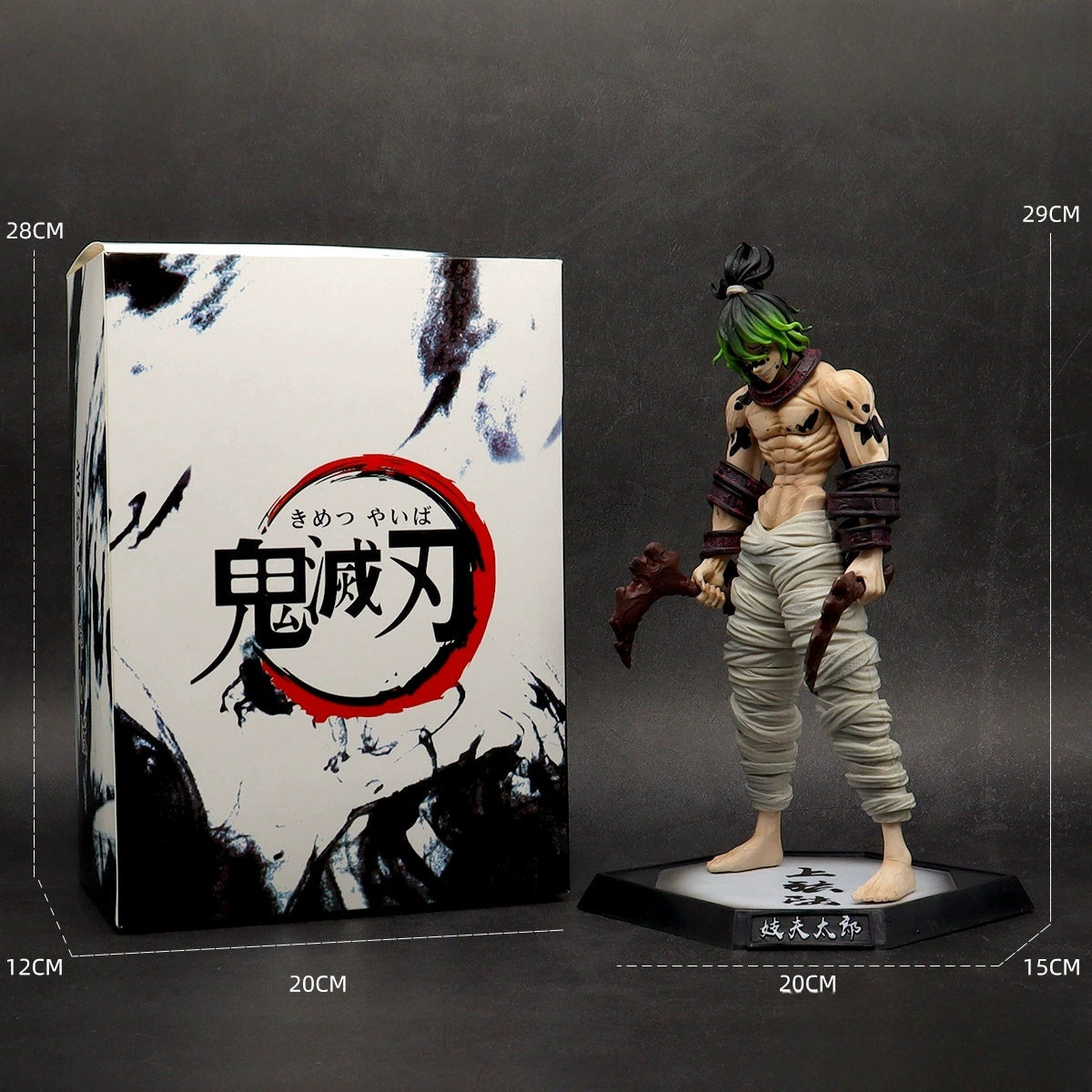 A striking Gyutaro Demon Slayer figure with a muscular build and green hair stands beside a white box decorated with black and red Japanese designs. The collectible features tattered pants. Box dimensions: 28x20x12cm; figure dimensions: 29x20x15cm.