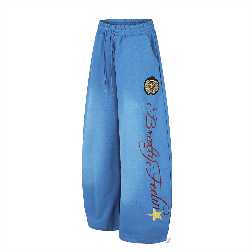 Blue wide-leg sweatpants angled front view with crest badge and script embroidery