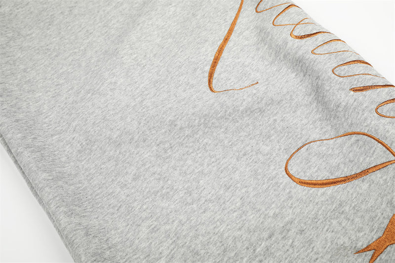 Close-up of gray sweatpants leg with brown script embroidery and heathered fabric texture