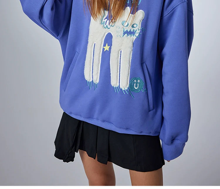 Wearing Seakoff's "Oh No! I Don’t Want to Work!" oversized graphic hoodie, featuring a cute lazy cat design, someone pairs it with a black pleated skirt. This casual streetwear look stands out against the plain white background, highlighting its playful charm.