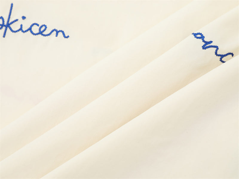 Cream shirt sleeve and side panel close-up with blue script embroidery