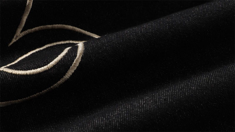 Close-up of black denim fabric with pale embroidered flame lines and textured weave