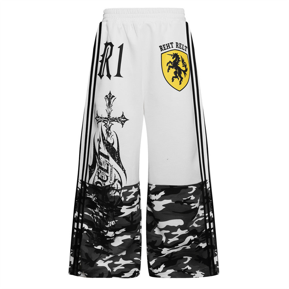 Men's wide-leg track pants in white with camo lower panel, gothic cross graphic print, unicorn shield logo, and triple side s