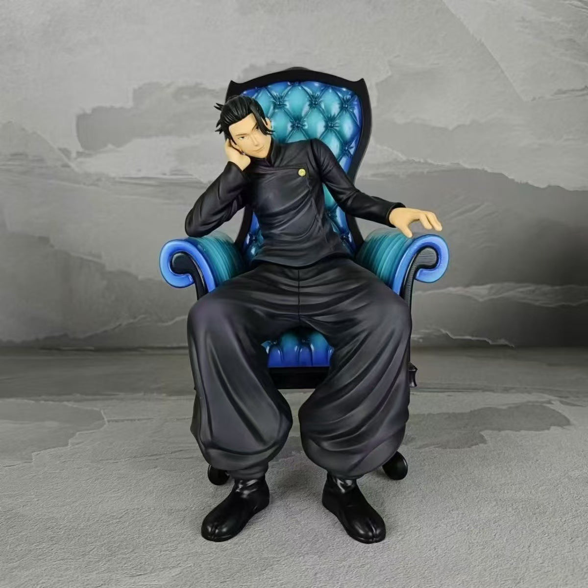 The Jujutsu Kaisen Satoru Gojo &amp; Suguru Geto Sitting Posture PVC Figure Set features a character with black hair lounging on a blue and black ornate chair, wearing loose-fitting pants and boots, exuding relaxation with their head resting on one hand against a plain gray background.