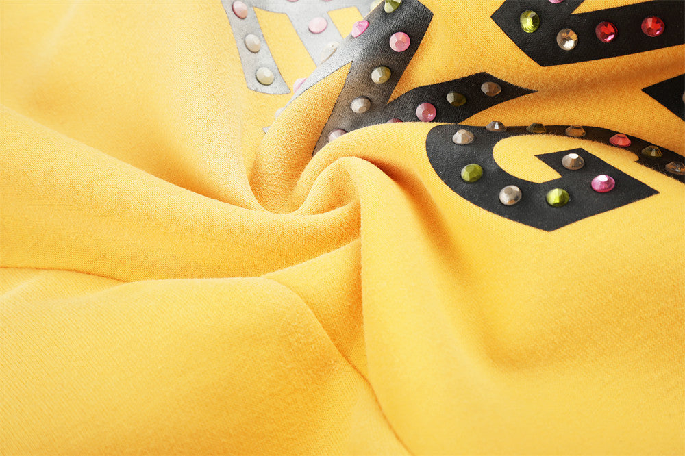 Close-up of rhinestone letter print and gathered fabric on yellow sweatpants