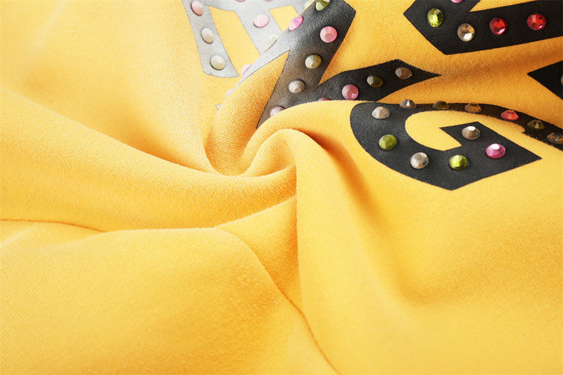 Close-up of rhinestone letter print and gathered fabric on yellow sweatpants