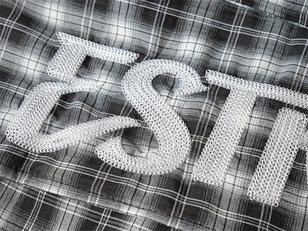 Close-up of large white embroidered letters on black plaid shirt back