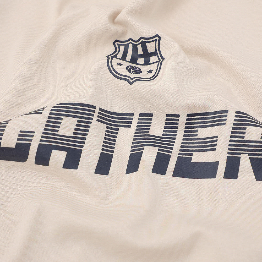 Close-up of GATHER chest print and small crest graphic on cream fabric
