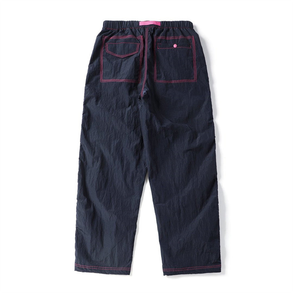 Back view of navy parachute pants featuring two outlined rear pockets with pink stitching