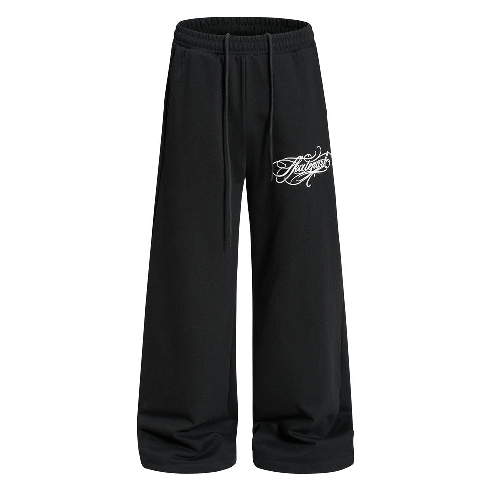 Wide-leg black sweatpants with white gothic script logo print on left thigh, elastic drawstring waist, relaxed straight-leg f