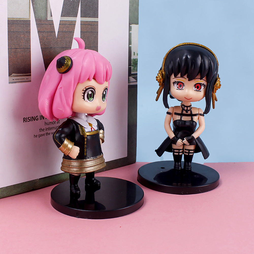 The Spy × Family 6-Piece PVC Figure Set includes anime-style figurines on black stands. One features pink hair and a black &amp; white outfit with gold accents, while another has black hair in similar attire, set against a pink and gray backdrop—ideal for collectors.