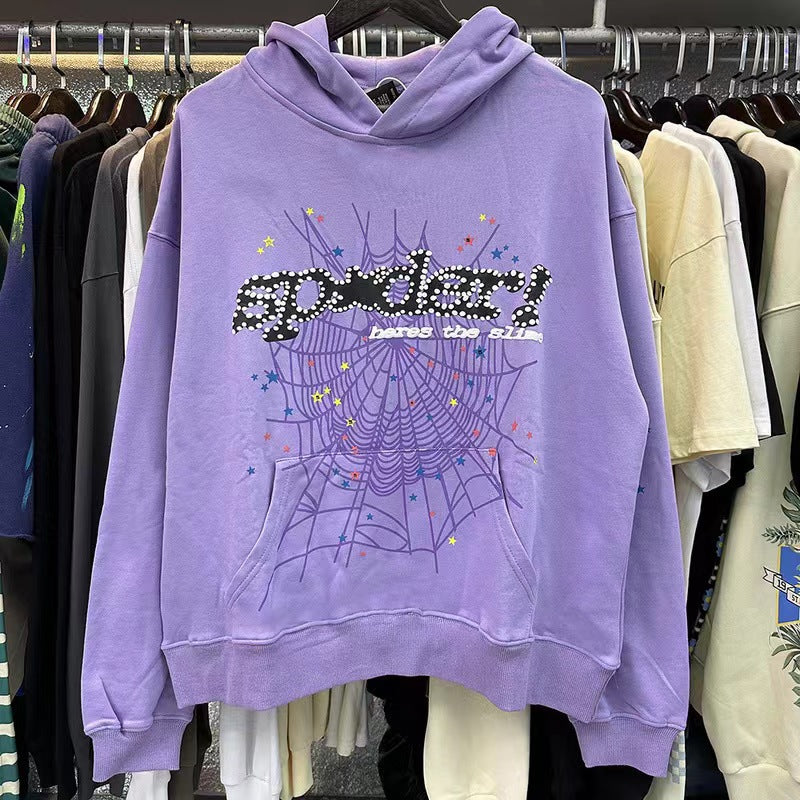 The Chic Purple Sp5der Hoodie by Sp5der features a trendy web and star print with stylized &quot;Sp5der&quot; text. Perfect for streetwear lovers, this hooded sweatshirt is displayed among other clothing items in the store.