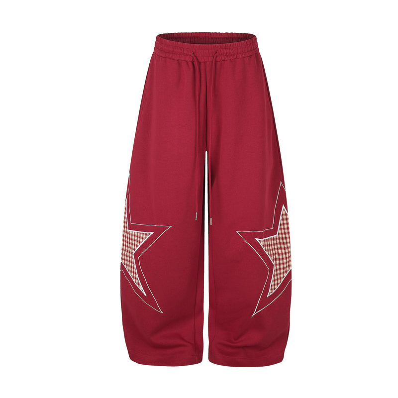 Oversized wide-leg sweatpants with large plaid star appliqué on each leg, shown in deep red with elasticated drawstring waist