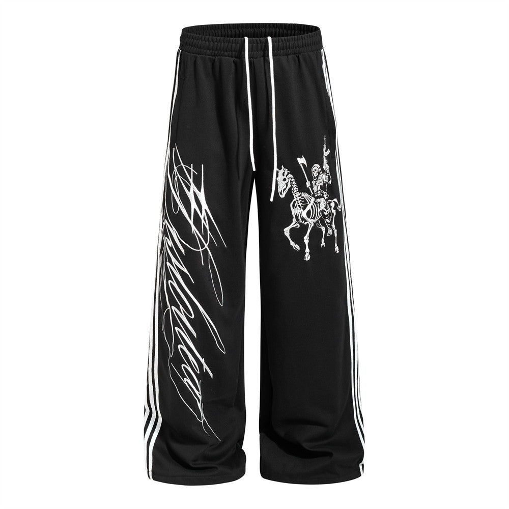 Wide-leg black track pants with skeleton rider graphic and three-stripe side tape detail