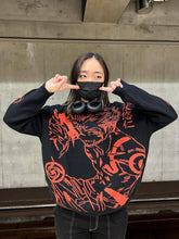 In front of a concrete wall, a person dons the Jujutsu Kaisen Premium Knit Sweater featuring Yuji Itadori & Nobara Kugisaki. With long hair, black mask, and headphones around their neck, they point at their eyes with both hands.