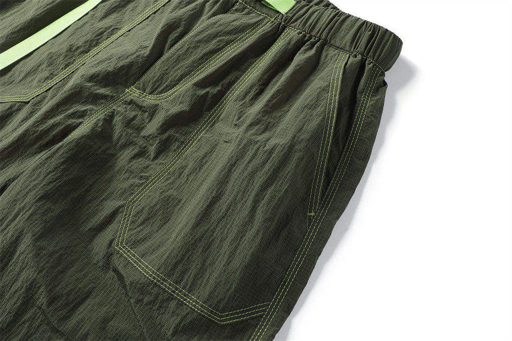 Close-up of an olive parachute pants cargo pocket with curved seams and bright green stitching