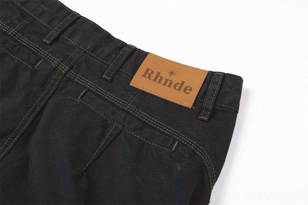 Close-up of back waistband corner on black pants with tan brand patch and stitched pocket