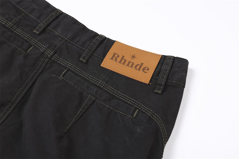 Close-up of back waistband corner on black pants with tan brand patch and stitched pocket
