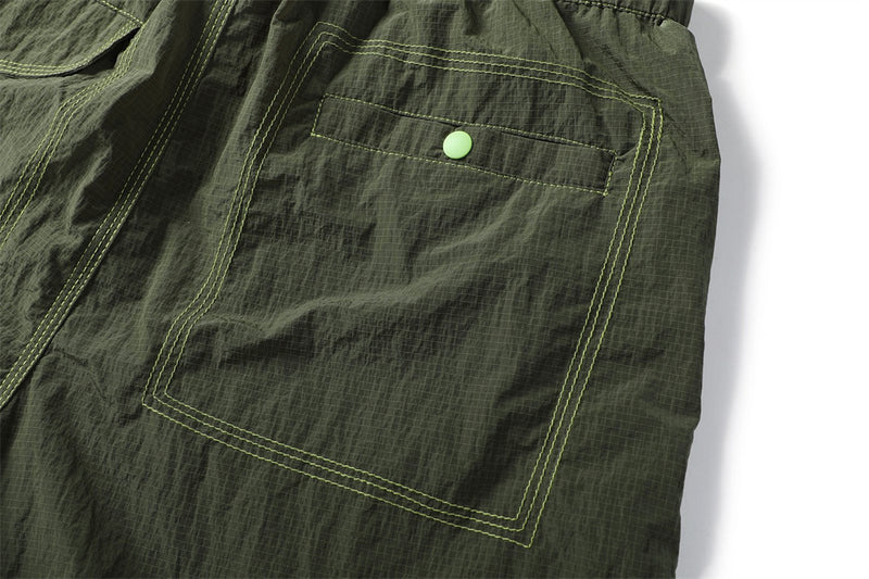 Detailed view of an olive rear pocket with double stitching and a bright green snap button