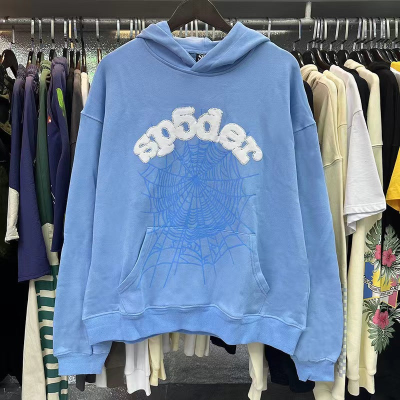 The Elegant Light Blue Sp5der Hoodie by Sp5der, featuring a trendy web print and &quot;sp6der&quot; on the front, stands out among vibrant hoodies in a streetwear fashion store.