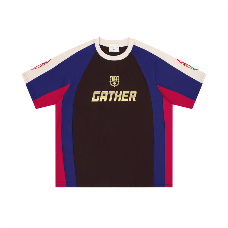 Men's colorblock soccer-style GATHER graphic tee in dark brown, blue, and crimson colorblock with crest badge and crew neck