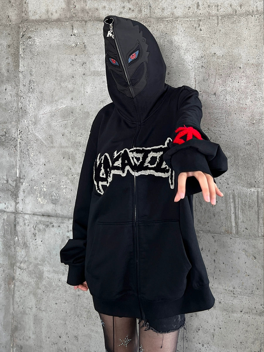 A person stands against a concrete wall in a Berserk-Inspired Griffith Dark Knight Hoodie, with its stylized front graphic. The hood obscures their face except for two red eyes on the mask. An arm extends forward, revealing a fingerless glove adorned with a red symbol.