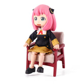 The Anya & Yor Forger Nendoroid Set from Spy × Family features a 13CM poseable figure with pink hair, large green eyes, a cheerful expression, and dressed in black and yellow. It sits on a red and beige chair wearing black shoes, embodying the iconic Nendoroid style.