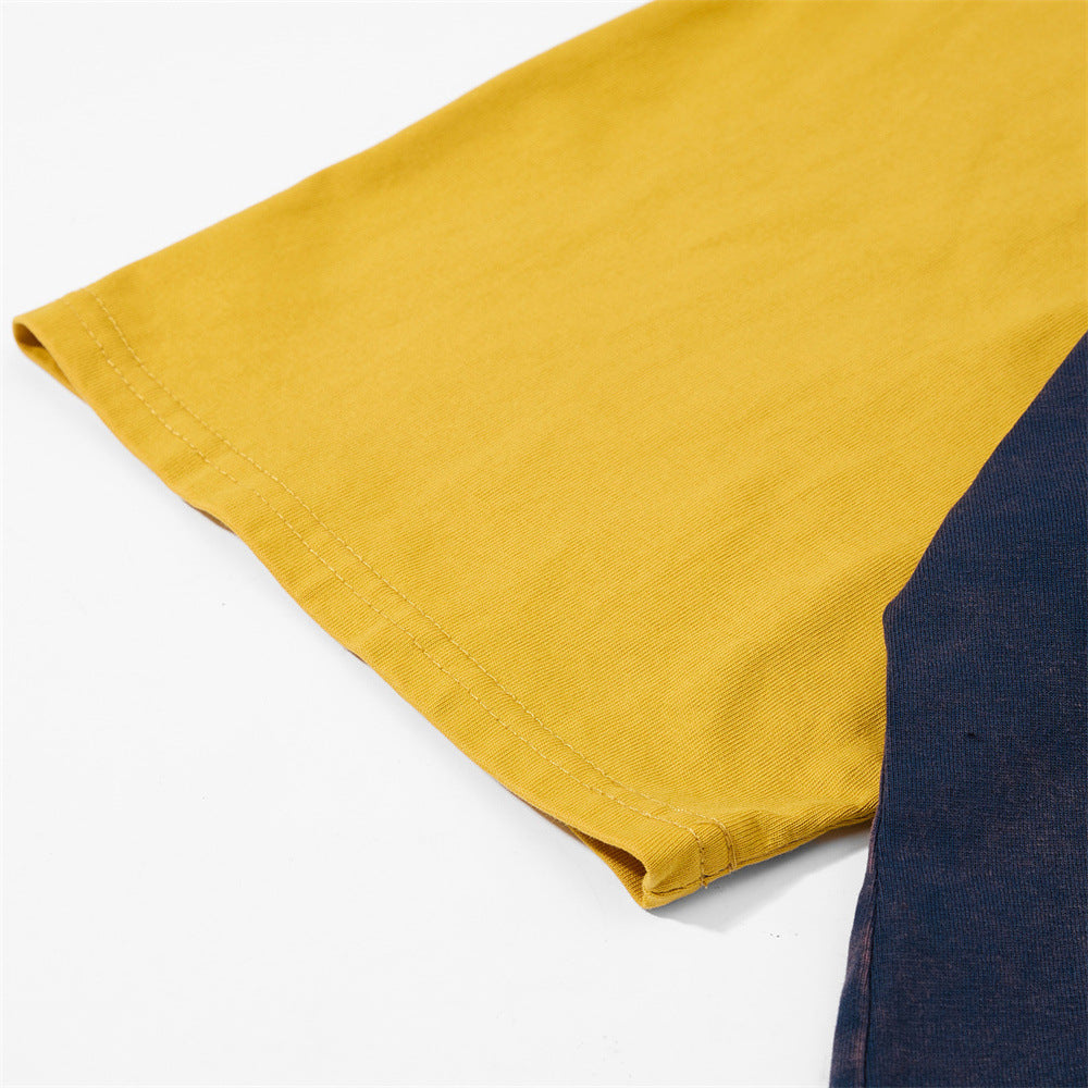 Close-up of a mustard yellow raglan t-shirt sleeve with navy colorblock detail and stitched hem