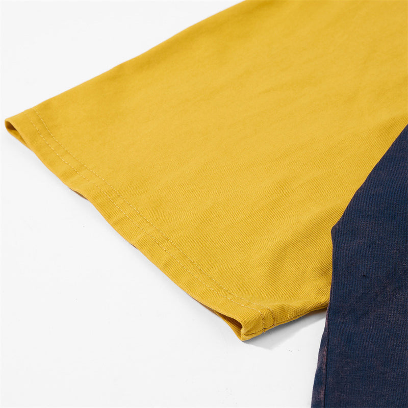 Close-up of a mustard yellow raglan t-shirt sleeve with navy colorblock detail and stitched hem